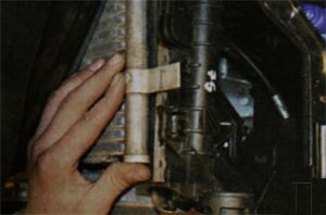 Немного опустив радиатор системы охлаждения извлеките из держателей на его бачках кронштейны радиатора системы кондиционирования и снимите с автомобиля радиатор системы охлаждения в сборе с электровентилятором